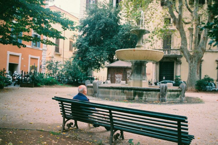persona mayor sentada en un banco en una plaza vacía