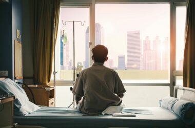 hombre de espaldas sentado en una habitación de un hospital mira a través de una ventana
